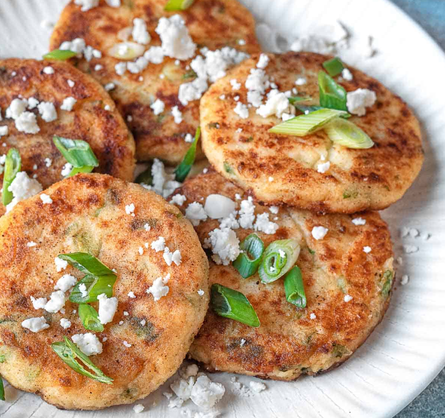 A plate of golden-brown mashed potato pancakes topped with sour cream and garnished with fresh chives.