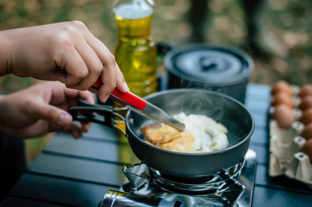 Hands cooking a meal on a lightweight camping stove with ingredients like eggs and olive oil, perfect for backpacking trips.