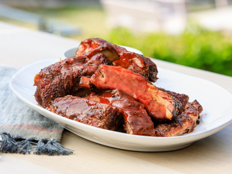 Plate of smoked barbecue ribs glazed with rich barbecue sauce, served on a white plate with a blurred outdoor background.