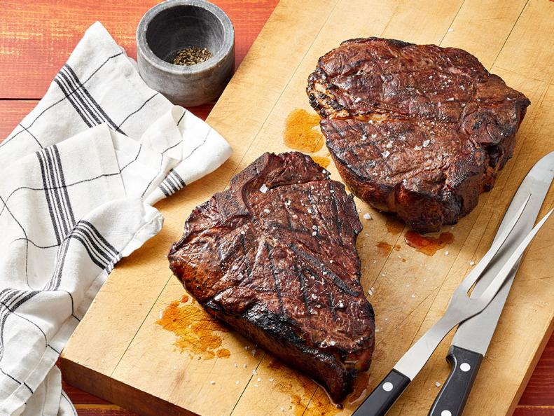 Perfectly smoked steaks on a cutting board, showcasing smoker recipes with coarse salt seasoning, a kitchen towel, and steak knives