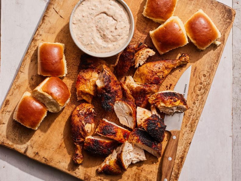 Smoked chicken pieces served on a wooden cutting board with soft dinner rolls and a bowl of creamy dipping sauce.